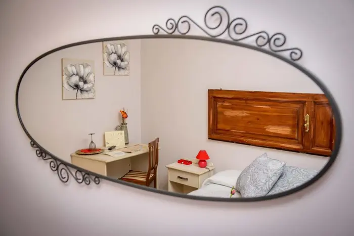 La camera riflessa nello specchio ovale in ferro battuto: scrivania, letto e testiera
